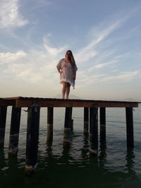 Low angle view of woman standing on pier over sea against sky