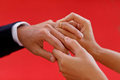 Cropped image of wedding couple exchanging ring against red background