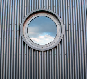 Cloudy sky reflecting in circle shaped mirror on corrugated iron