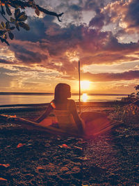 Man sitting on beach against sky during sunset