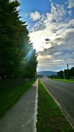 Road passing through field against cloudy sky