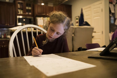 Cute blonde girl with french braids works on school papers at home