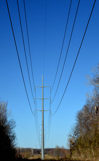 Low angle view of electricity pylon against clear blue sky