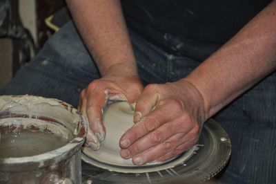 Midsection of man shaping pot on pottery wheel