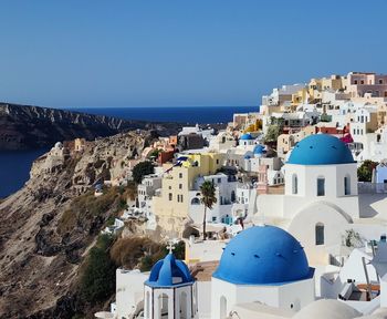 Buildings by sea against clear blue sky