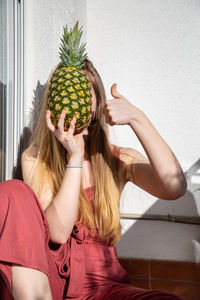 Young woman holding pineapple against wall in balcony