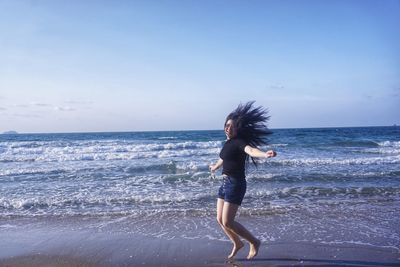 Full length of young woman at beach against sky