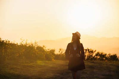 Woman standing on field against sky during sunset