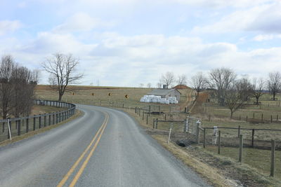 Empty road amidst amish field against sky