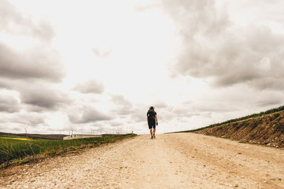 Rear view of man walking on road against cloudy sky
