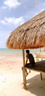Rear view of man sitting in hut at beach