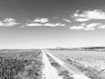 Dirt road amidst field against sky