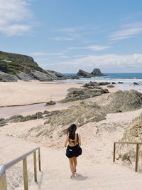 Rear view of woman standing at beach against sky