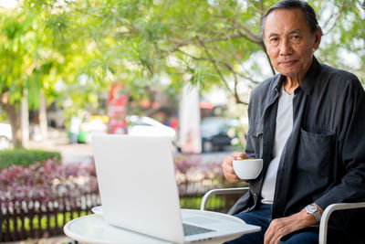 Portrait of man with laptop sitting by table at caf�