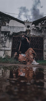 Reflection of man sitting in abandoned building against sky