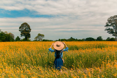 Rear view of young woman standing in yellow flower field 