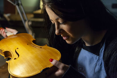 Young woman apprentice violinmaker checking the beauty of her violin