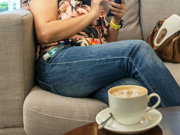 Midsection of woman with coffee cup sitting on sofa