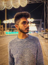 Young man looking away while standing on illuminated road