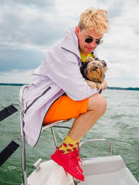 Handsome person sitting on a sailing yacht and hold his small dog yorkshire terrier during vacations