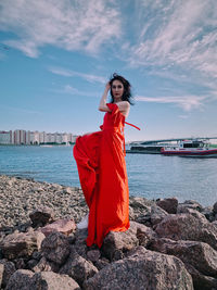 Young woman standing on rock by sea against sky