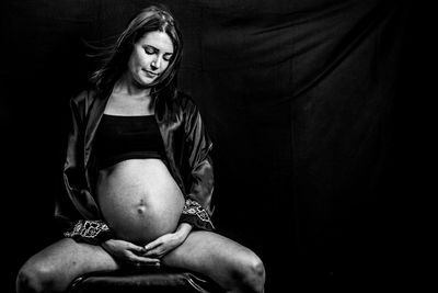 Pregnant woman sitting against on chair black background