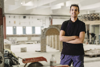 Portrait of confident carpentry student standing arms crossed at workshop