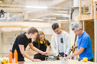 Male instructor explaining power drill on plank to trainees at workbench