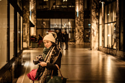 Portrait of mature woman with digital camera standing in corridor