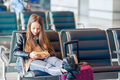 Girl using mobile phone while sitting at airport