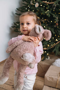 Happy child received christmas present stuffed toy near tree at home. kid getting gift 