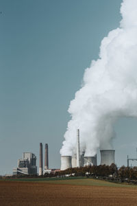 Smoke emitting from factory against clear sky