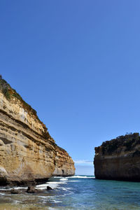 Rock formations on shore against clear blue sky
