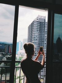 Rear view of woman standing by window in city