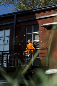 Woman in orange dress sitting cross-legged on railing