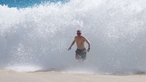 Shirtless man wearing sunglasses running in sea