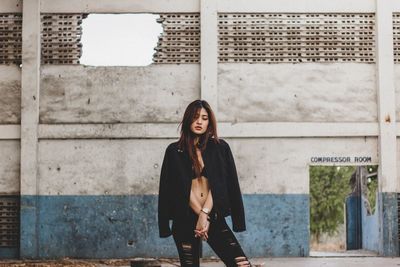 Fashionable young woman standing against old weathered wall