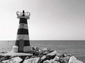 Lighthouse by sea against clear sky