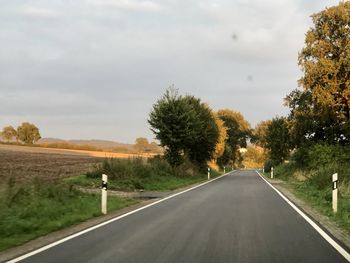 Road by trees against sky