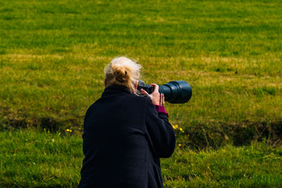 Rear view of woman photographing with camera while standing on grassy field
