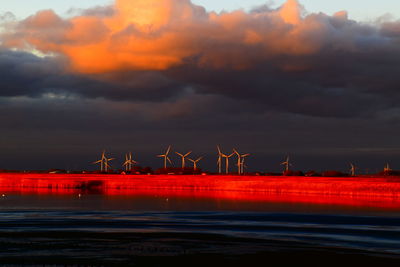 Scenic view of sea against sky during sunset and white windmills on the horizon.