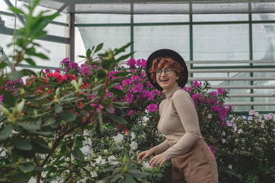 A beautiful plus size girl in a hat laughs among the green plants of the greenhouse.