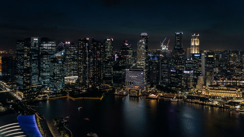 Illuminated city by river against sky at night