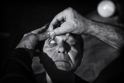 Cropped hands of man putting eyedrops in eye