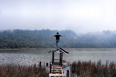 Man standing on gazebo by lake against sky