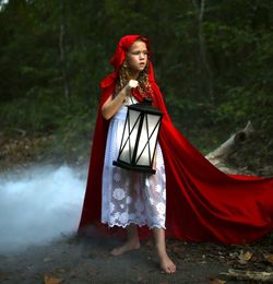 Full length of girl holding lantern while standing in forest