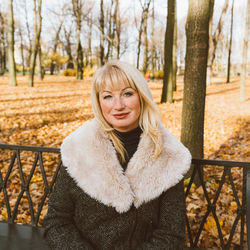 Portrait of smiling mature woman sitting on bench at park during autumn