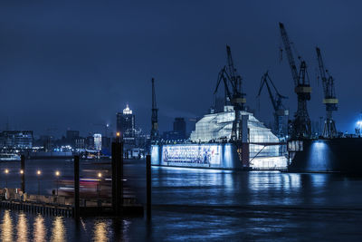 Illuminated commercial dock by sea against sky at night