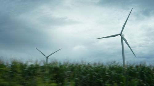 Wind turbines in field against sky during foggy weather