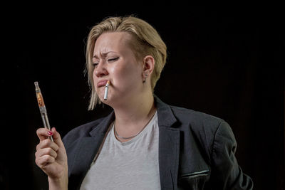 Sad young woman with electronic cigarette against black background
